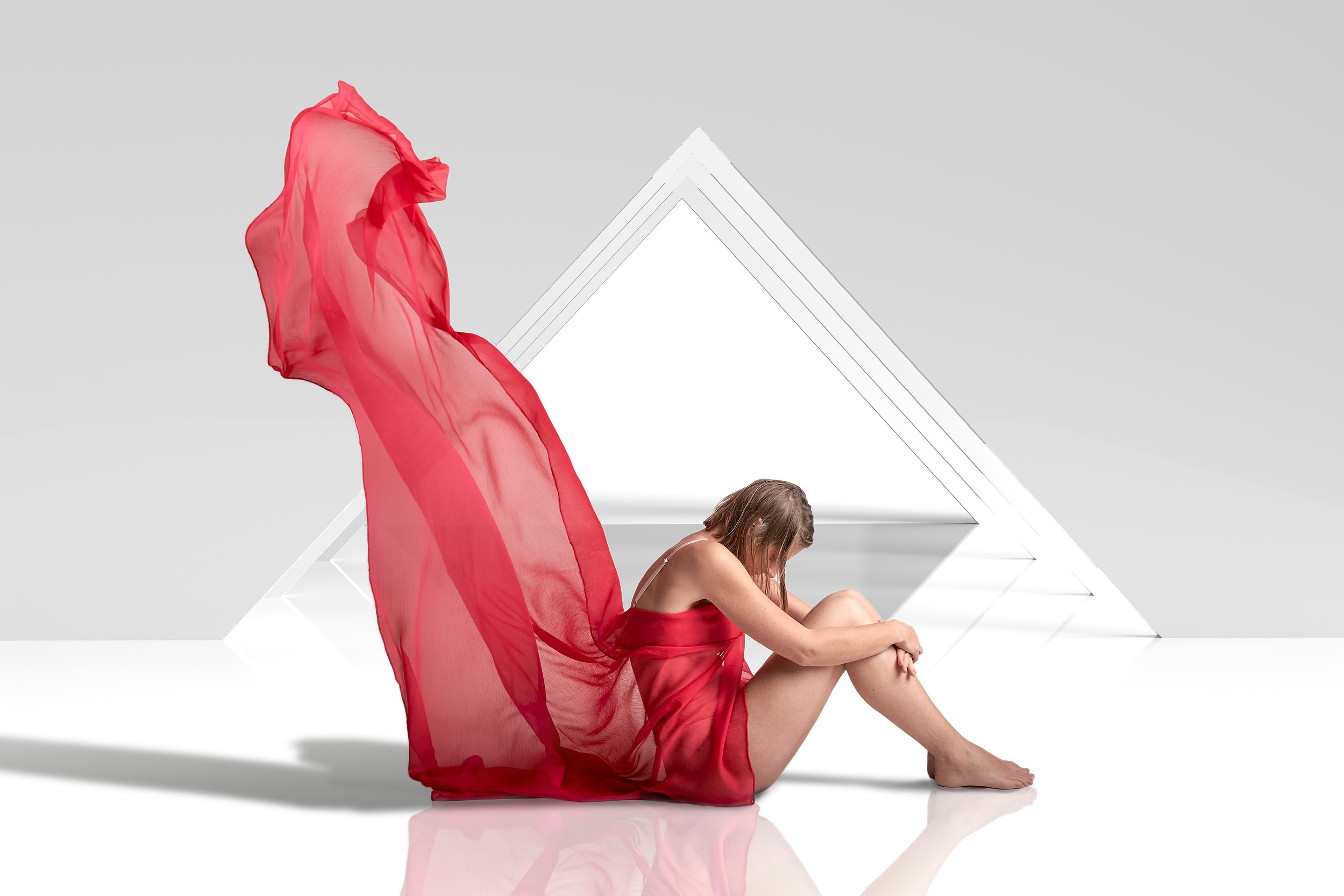 Seated figure wrapped in red fabric before a white triangular structure